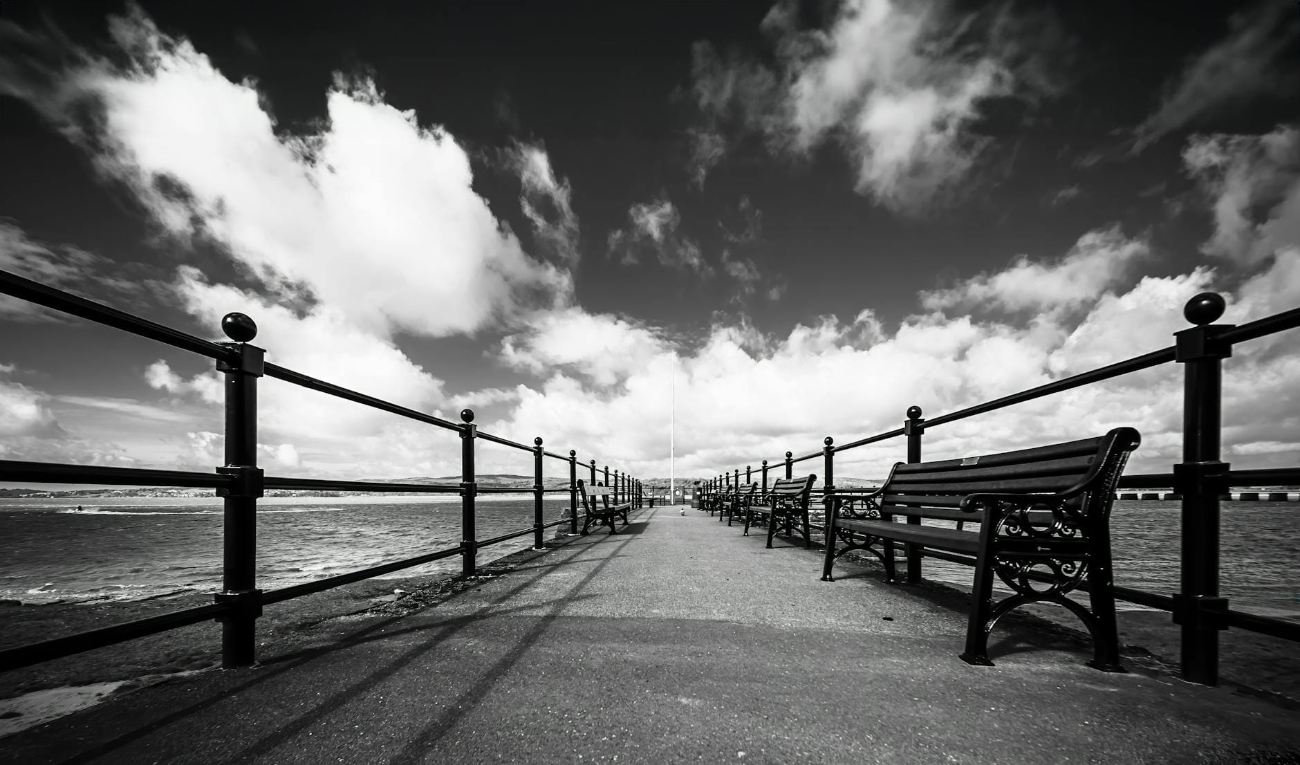 Ustka wiosną przed sezonem: pierwsze promienie słońca i puste ścieżki Czarno-biała promenada z ławkami i dramatycznymi chmurami nad morzem