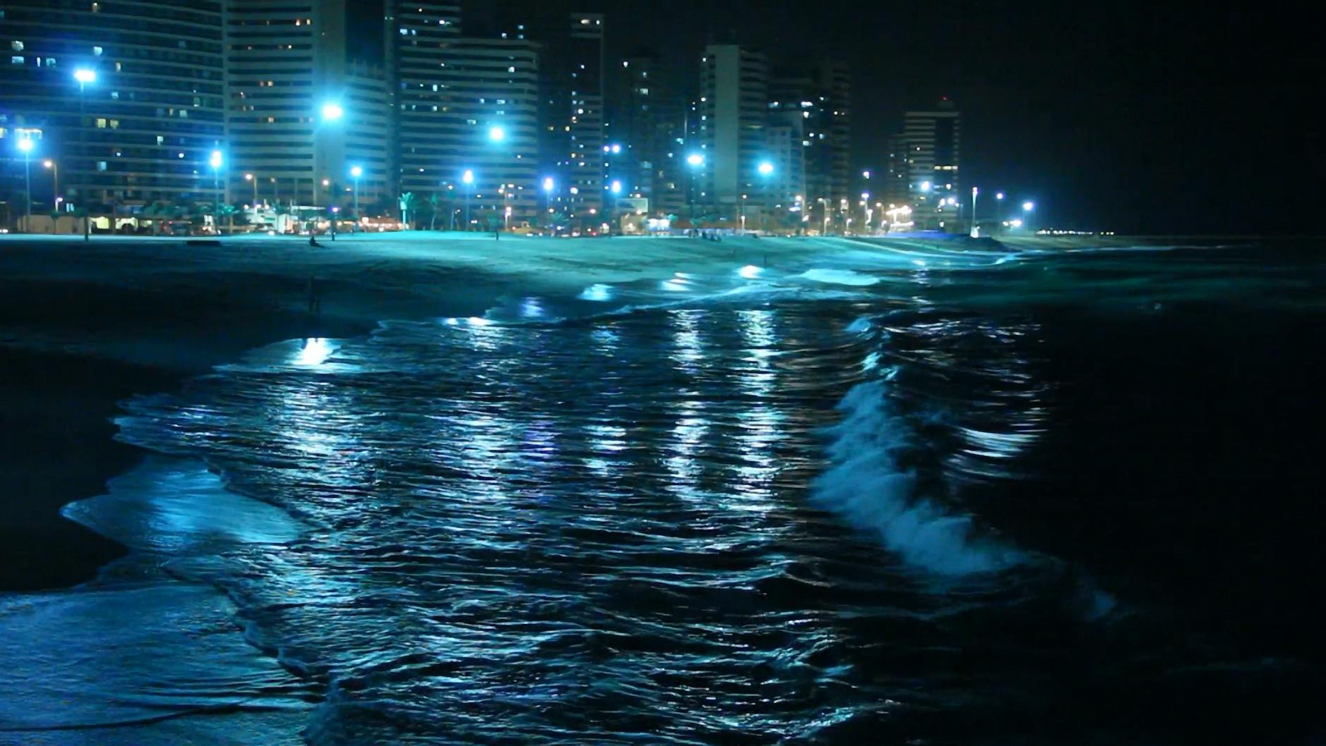 Nocne światła nadmorskiego miasta odbijające się w spokojnym morzu