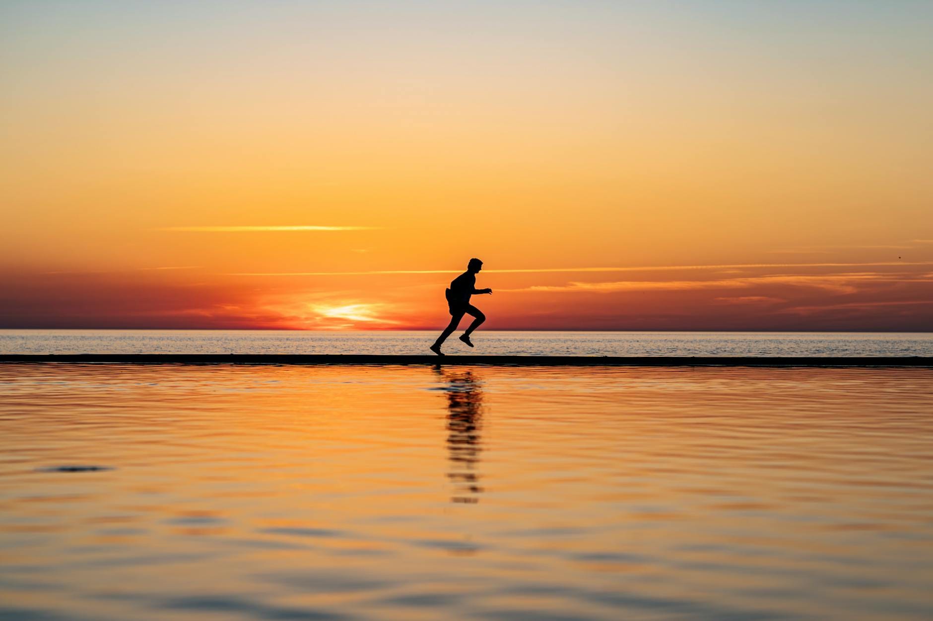 Biegacz w sylwetce biegnący po plaży o zachodzie słońca