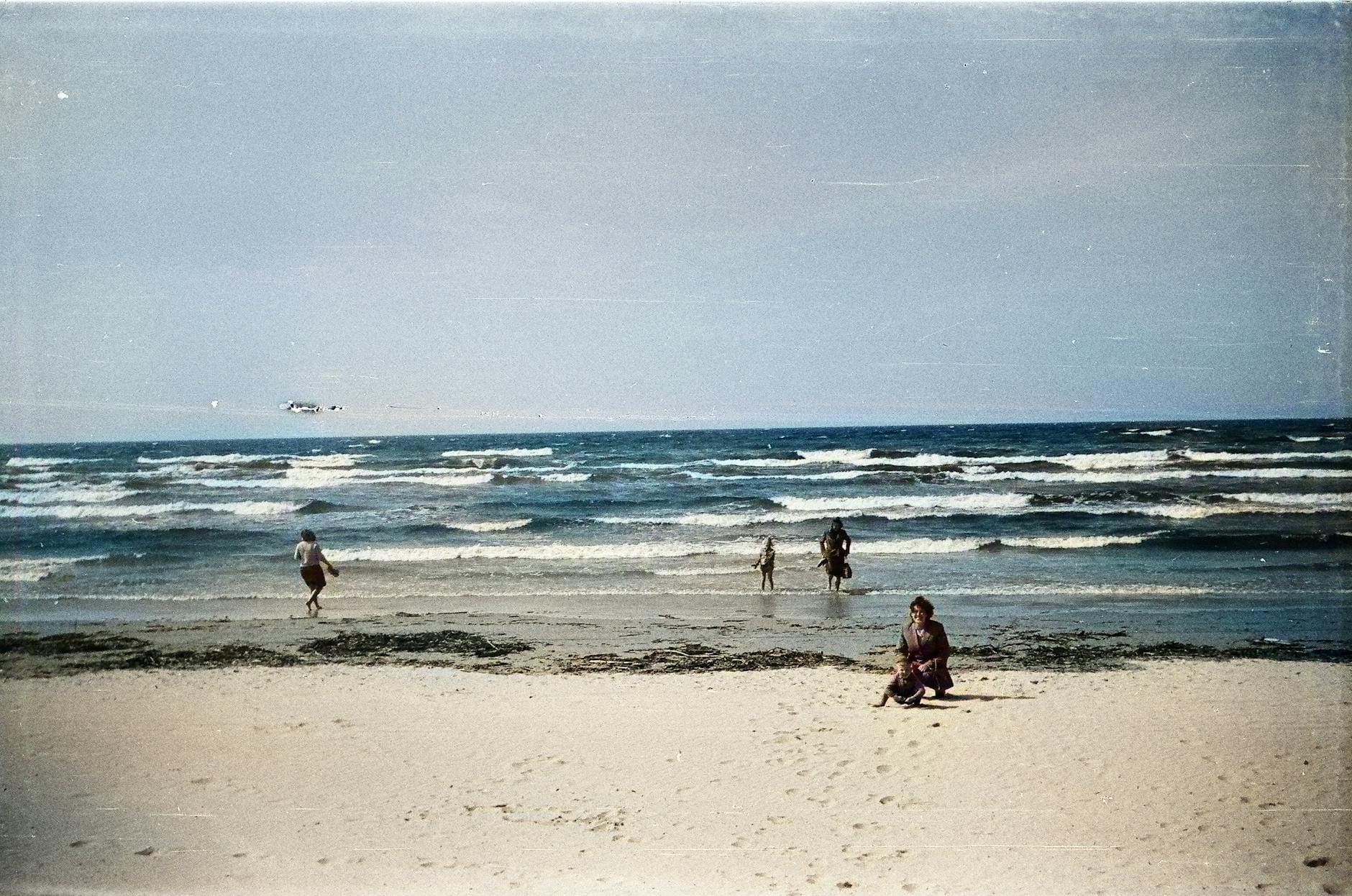 Rodzina spacerująca brzegiem spokojnej, piaszczystej plaży nad morzem