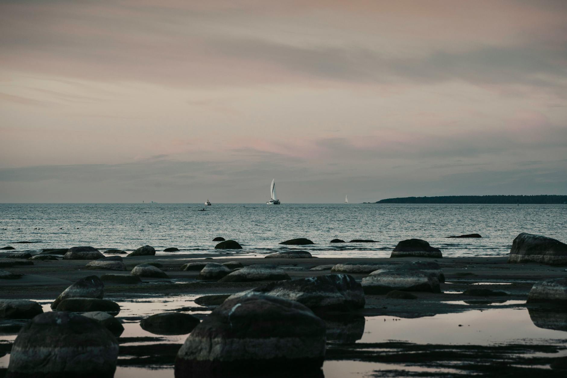 Zachód słońca nad Bałtykiem z kamienistym brzegiem i żaglówkami